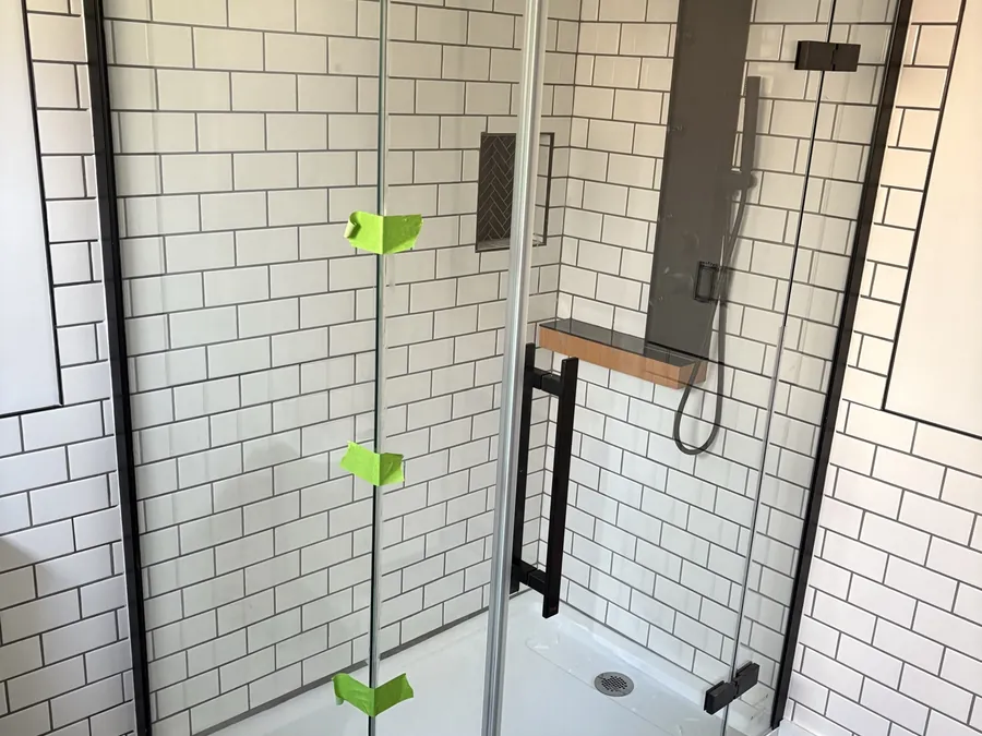 A walk-in shower tiled in white subway tile with a black herringbone floor and matte black fixtures.